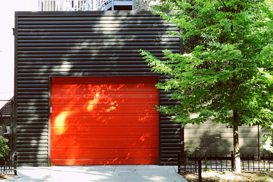 red garage door with a black facade house and a tree outside
